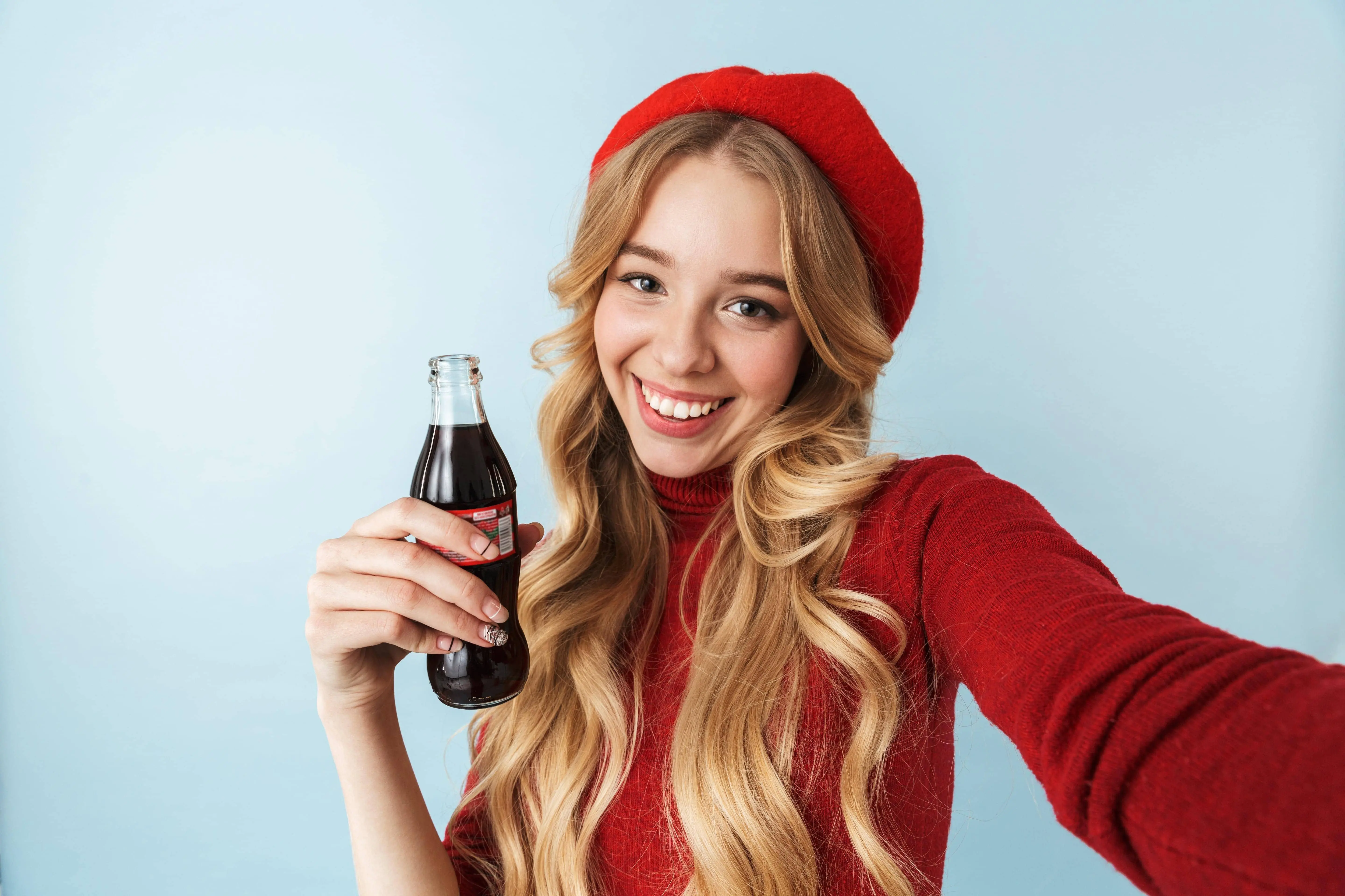 Mujer joven sosteniendo una botella de Coca-Cola y sonriendo en una selfie.